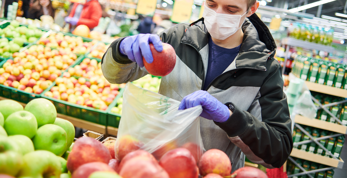 Homem com máscara escolhendo maçãs em um supermercado